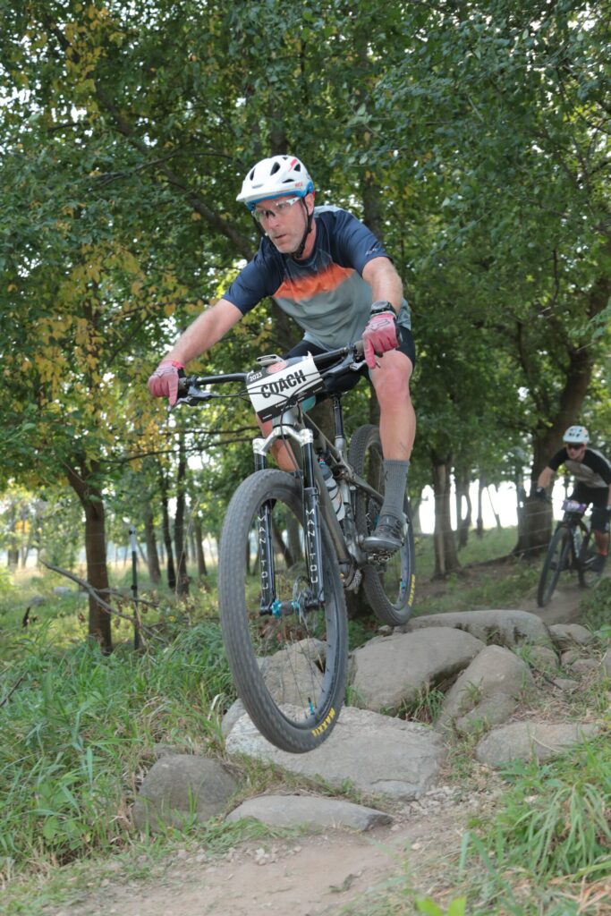 Coach riding a rock garden on a mountain bike course with a rider following